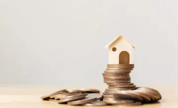 Casa de madera sobre una pila de monedas, simbolizando el ahorro y la inversión en vivienda, en el contexto de la ley subsidio, que promueve el acceso a la vivienda para quienes necesiten apoyo económico