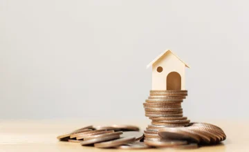 Casa de madera sobre una pila de monedas